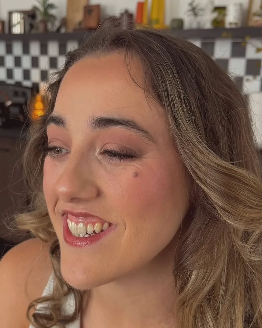 Event glam on a smiling client: shimmer lid, winged liner, soft pink lip.