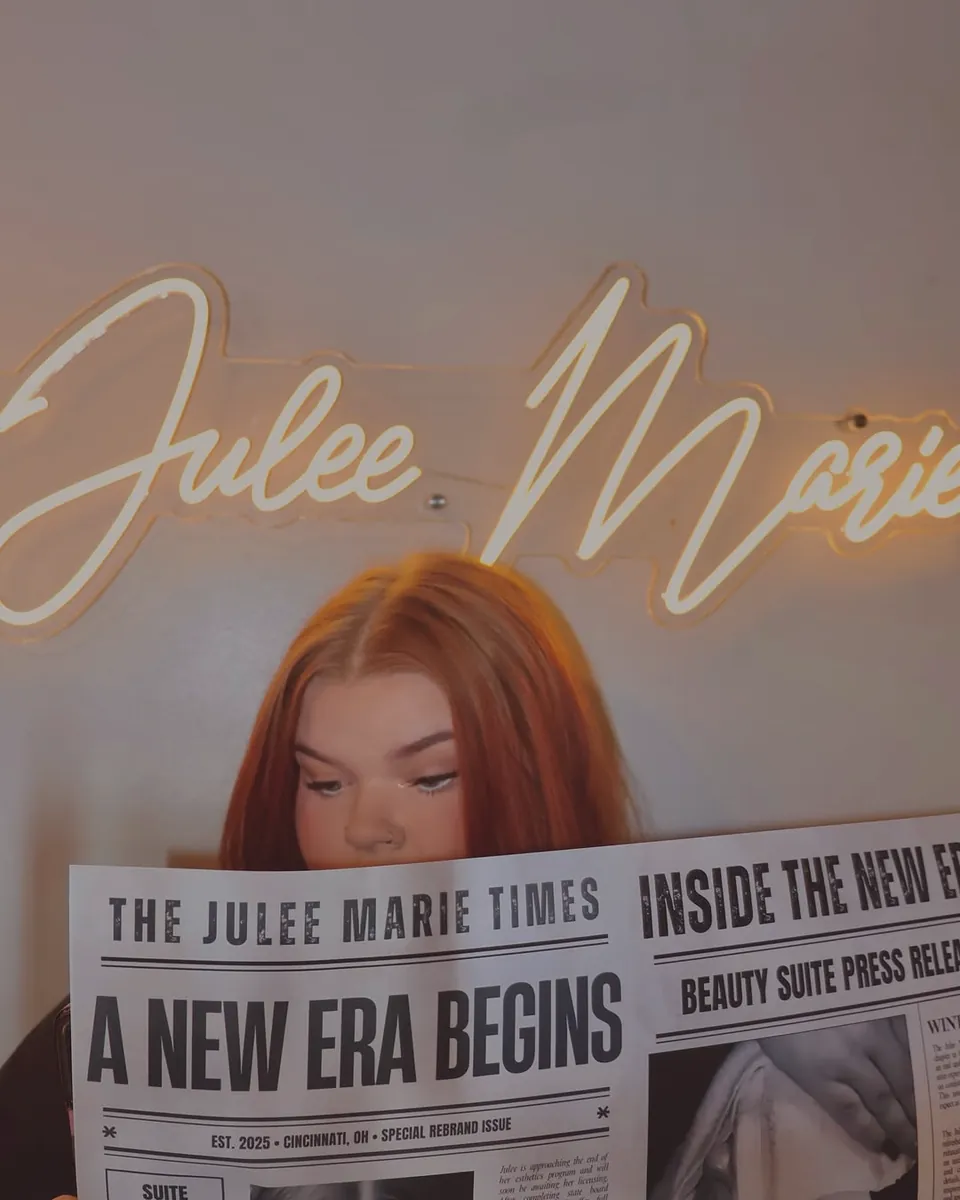 Julee Marie reading her own newspaper, The Julee Marie Times, under her name in neon.