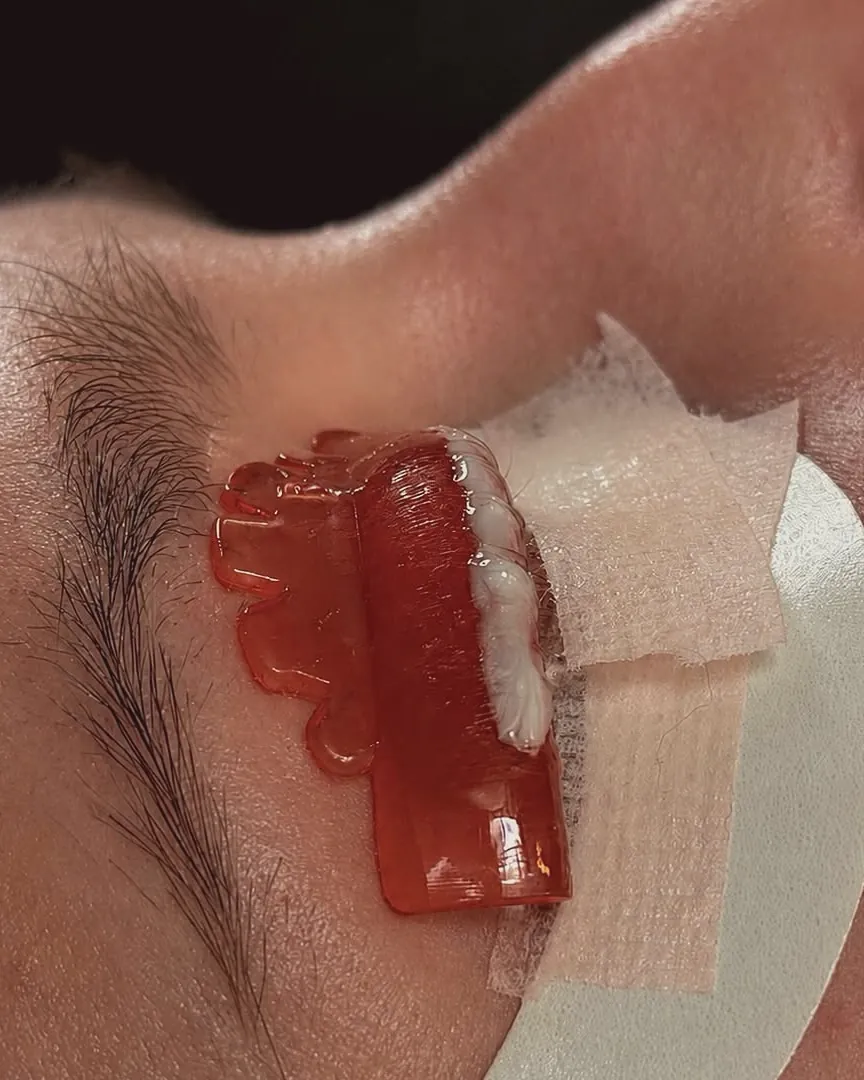 Close-up of red brow wax and a protective strip at the brow, mid-service.