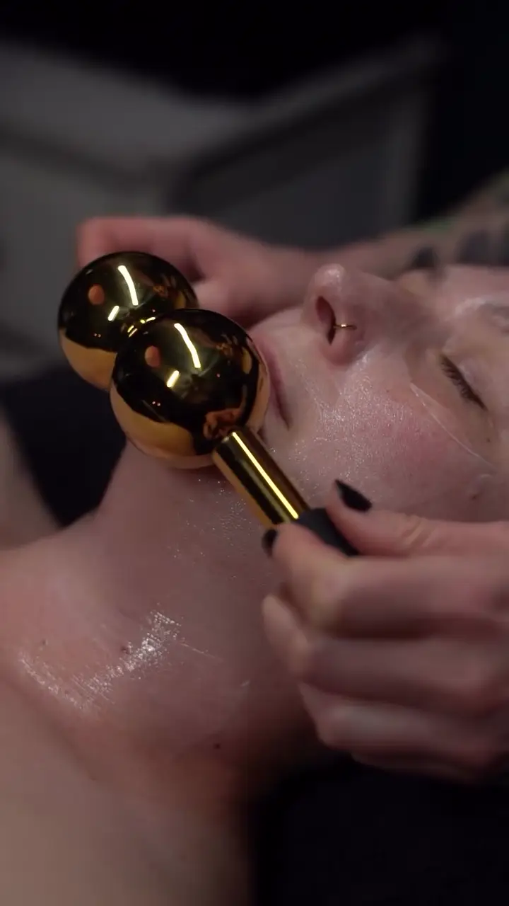Alaina’s hands guide gold globes along a client’s jaw.